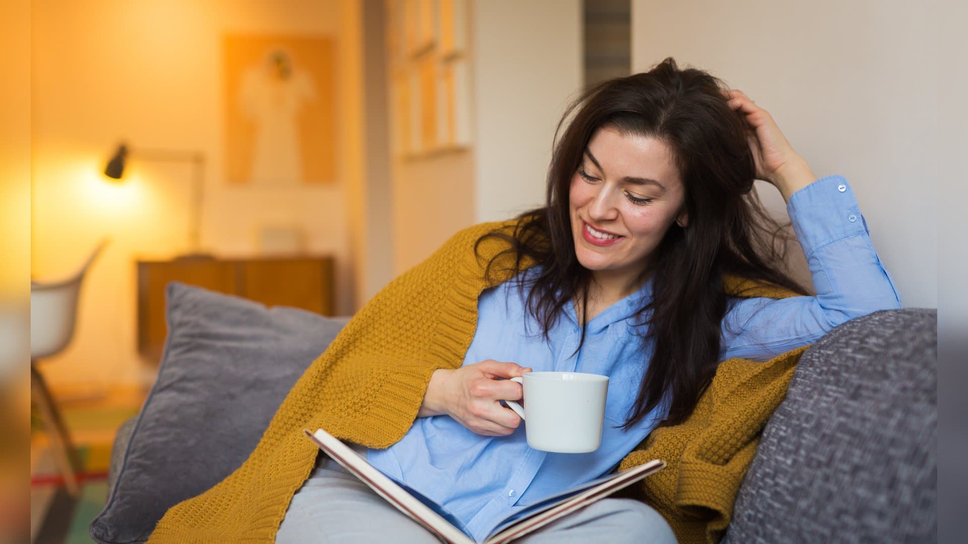 Ein gutes Buch in der Hand, eine dampfende Tasse Tee daneben: So kann man im Herbst viele Stunden auf dem Sofa verbringen. Auch diese Aktivitäten schaffen Wohlfühlatmosphäre in der kalten Jahreszeit.