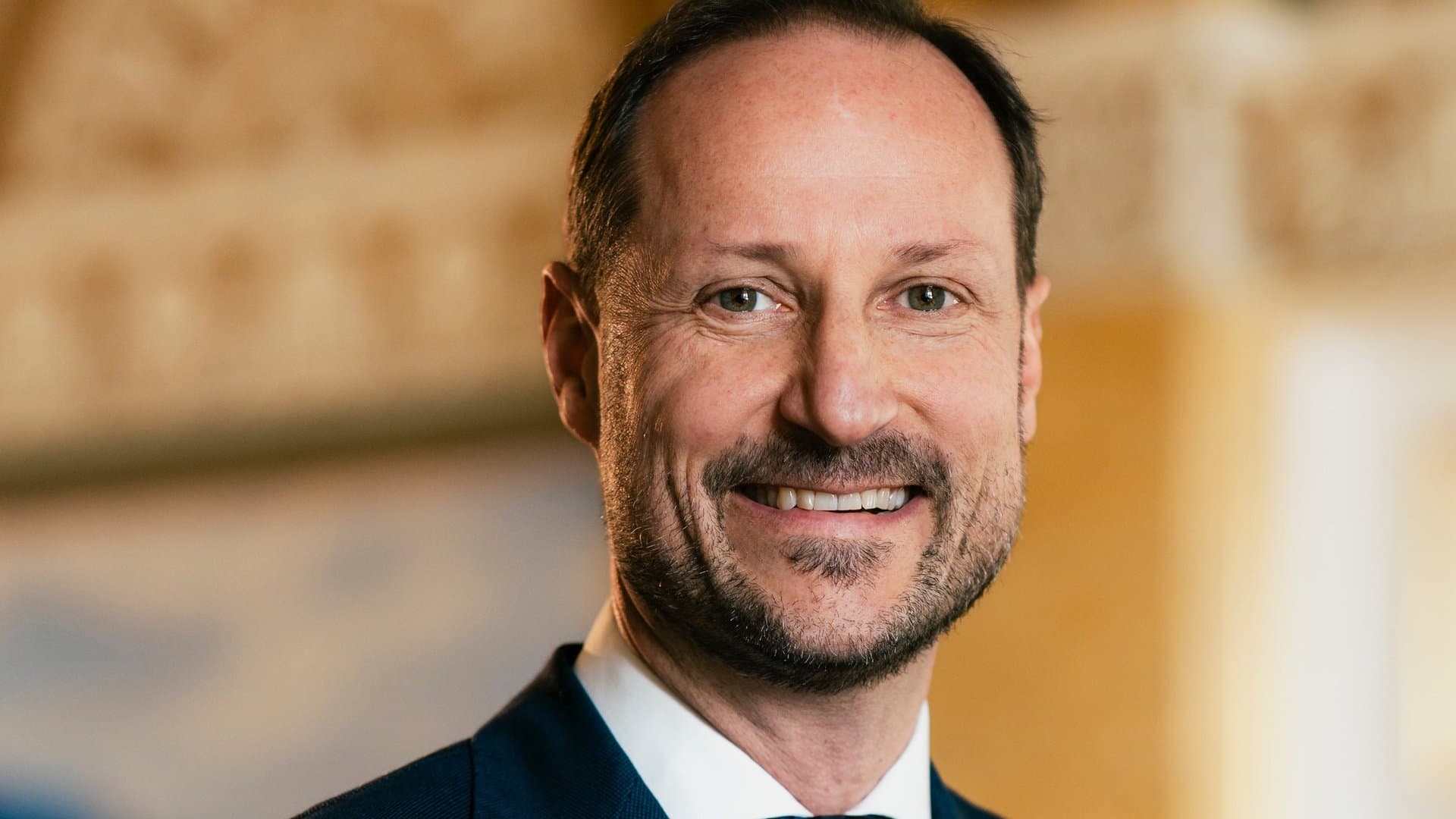 In the birthday photo, Crown Prince Haakon presents himself smiling and wearing a suit.